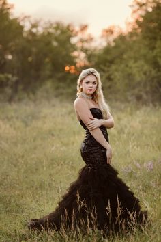 a woman in a long black dress standing in tall grass with her hands on her hips