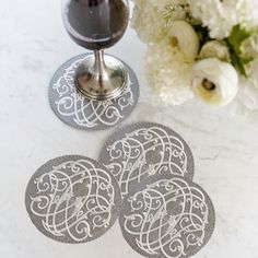 three coasters on a table next to a wine glass and flower vase with white flowers