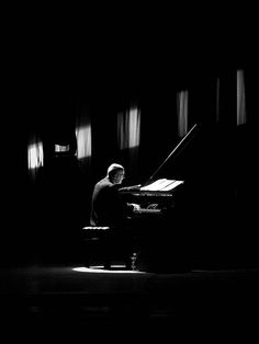 a man sitting at a piano in the dark with his head turned to the side