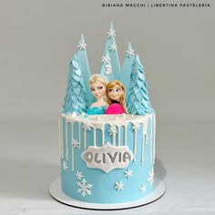 a frozen princess themed cake with two dolls on top and snow - covered trees in the background