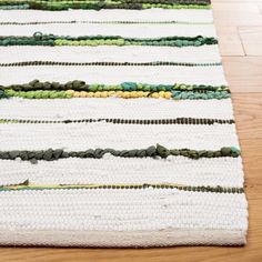 a white rug with green and yellow stripes on top of wooden floor next to wood flooring