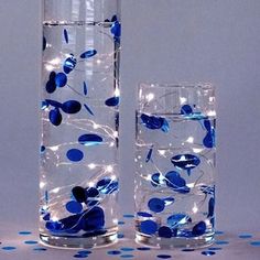 two clear vases with blue flowers and lights in them on a polka dot tablecloth