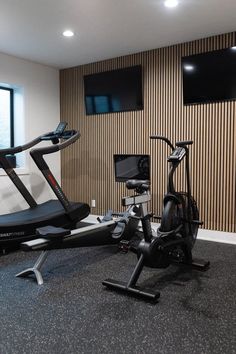 an exercise room with two stationary bikes and televisions on the wall behind them in front of a flat screen tv