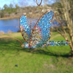 a blue glass butterfly hanging from a wire in front of a body of water and grass