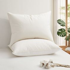 a white pillow sitting on top of a bed next to a plant