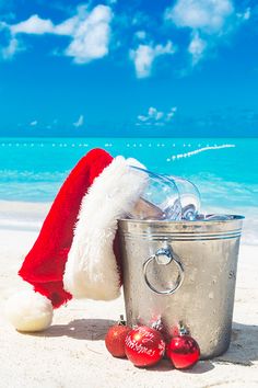 a santa hat sitting on the beach next to a trash can with christmas decorations in it