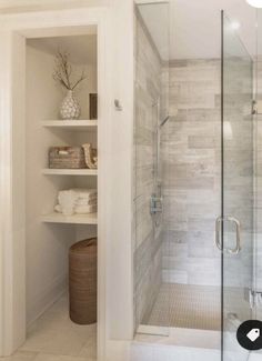 a walk in shower sitting next to a white shelf filled with towels and vases