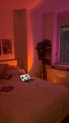 an open laptop computer sitting on top of a bed in a room with pink lighting