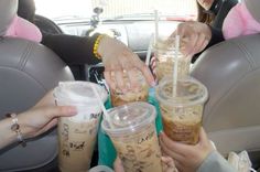 three people in the back seat of a car holding up iced coffees and drinks