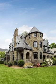 an old stone house with large windows and lots of greenery in the front yard