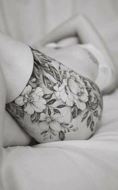 a woman laying on top of a bed covered in white sheets with flowers tattooed on her stomach