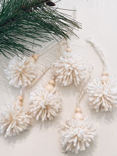 three white pom - poms are hanging from a pine branch on a table