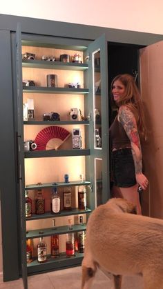 a woman standing next to a brown dog in front of a cabinet filled with liquor bottles