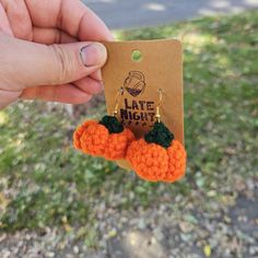 a person holding up a pair of orange and green crocheted earrings with the words late night written on them