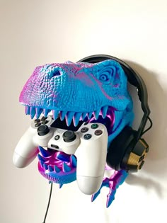 two video game controllers are hooked up to a wall mounted dinosaur head with purple and blue paint