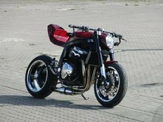 a black and red motorcycle parked on top of a brick road next to a parking lot