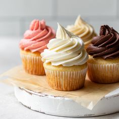 four cupcakes with white frosting on a wooden board