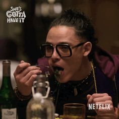 a man with glasses eating food at a table next to wine bottles and glassware