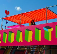 a woman standing on top of a colorful sign under a blue cloudless sky,