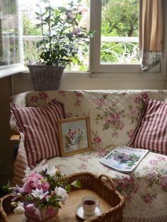 a couch with flowers and pictures on it in front of a window next to a table