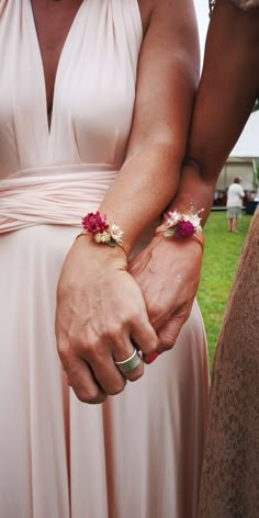 the bride and groom are holding hands with their wedding rings on their wrist, both wearing flower bracelets