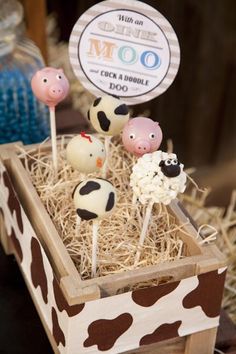 some cake pops are in a wooden box with hay and cow faces on them,