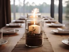 two lit candles sit in a glass jar on a table with plates and napkins