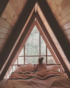 a woman sitting on top of a bed in a loft next to a tall window