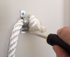 a person holding a screwdriver near a white wall with rope on the hook