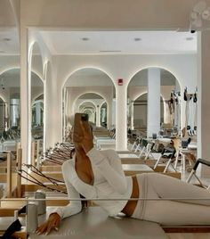 a woman taking a selfie while sitting on the floor in a gym with rows of treadmills