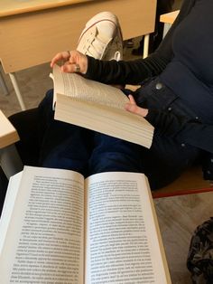 a person sitting down reading a book with their hands on top of the open book