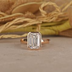 an emerald colored diamond ring sitting on top of a table next to a baguette