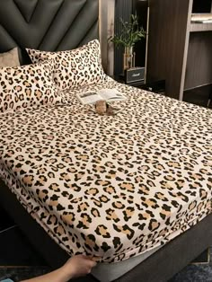 a bed with a leopard print comforter and pillows on top of it, next to a black headboard