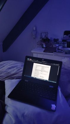 an open laptop computer sitting on top of a bed in a room with purple lighting