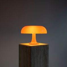 an orange lamp sitting on top of a wooden block in front of a gray wall