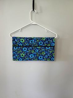 a blue and green flowered purse hanging on a white hanger against a wall