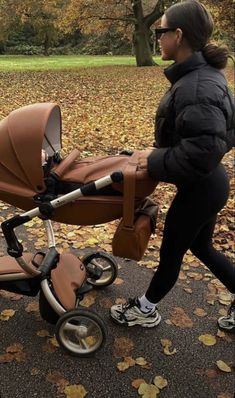 a woman pushing a stroller in the park with leaves on the ground around her