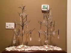 two metal trees with snowflakes on them in front of a wall mounted outlet