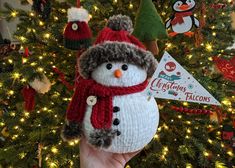 a hand holding a snowman ornament in front of a christmas tree