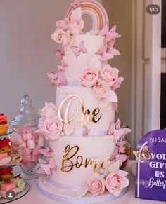 a three tiered cake decorated with pink flowers and gold lettering that says one bomb