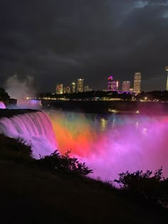 the niagara falls lit up in pink, purple and green at night with city lights