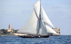 a sailboat with white sails sailing in the ocean next to an island and castle