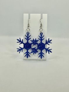 snowflake earrings with blue glitter on them sitting in front of a white box