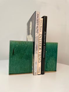 two books are stacked on top of each other in front of a white wall and green bookends