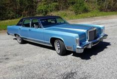 an old blue car is parked on the gravel