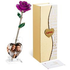 a purple rose in a clear vase next to a cardboard box with a photo inside