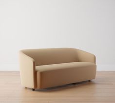 a tan couch sitting on top of a hard wood floor next to a white wall