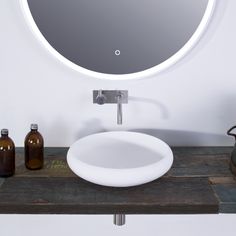 a bathroom sink with a round mirror above it and bottles on the counter top next to it