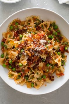 a white bowl filled with pasta, peas and sauce on top of a gray table