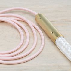 a pink and white braided cord with a gold handle on a wooden surface next to a lighter